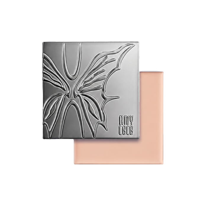 ANYCOCO cream foundation compact with embossed silver butterfly cover, shown over a peach-toned square case