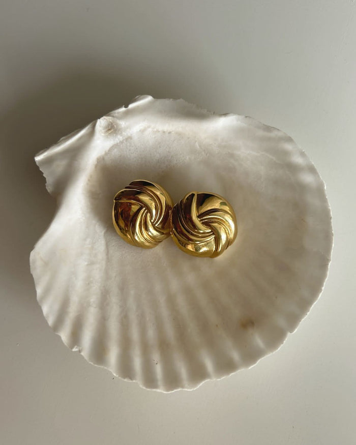 gold swirl earrings displayed on a white shell tray