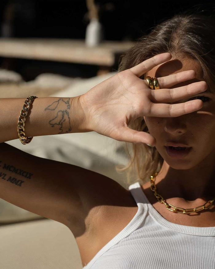 hand covering face featuring gold bracelet, necklace, and rings