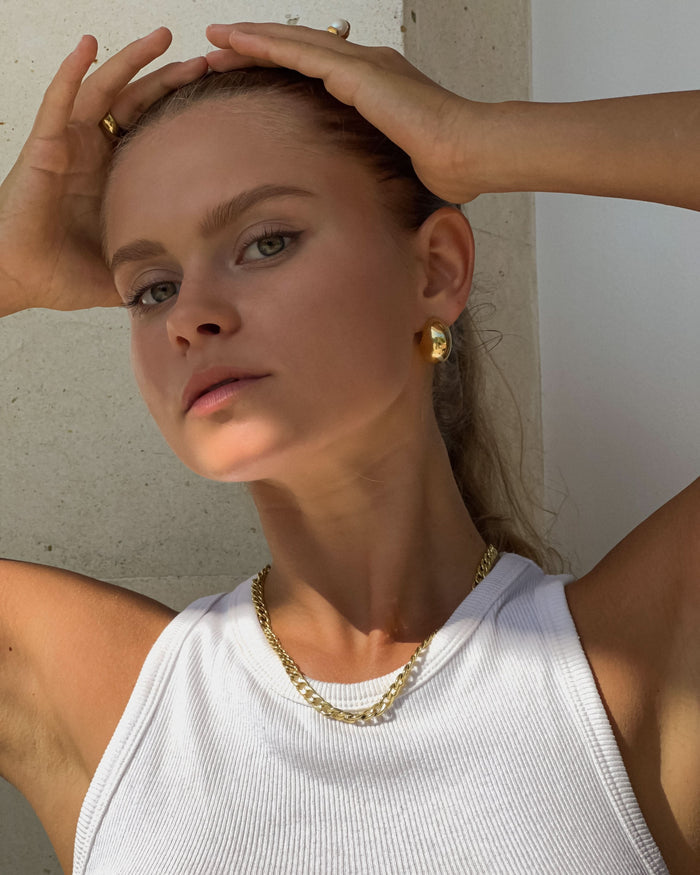 a glr in a tank top and gold earrings and necklace