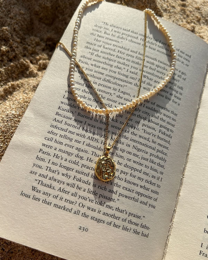 gold pendant necklace and pearl choker on top of the book