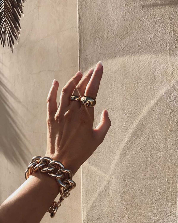 hand wearing chunky gold necklace and two dome rings