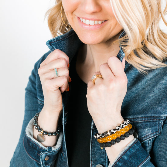 Woman wearing bracelet stack; black spotted giraffe agate with gold and CZ rings, polished honey citrine, and black lava rock