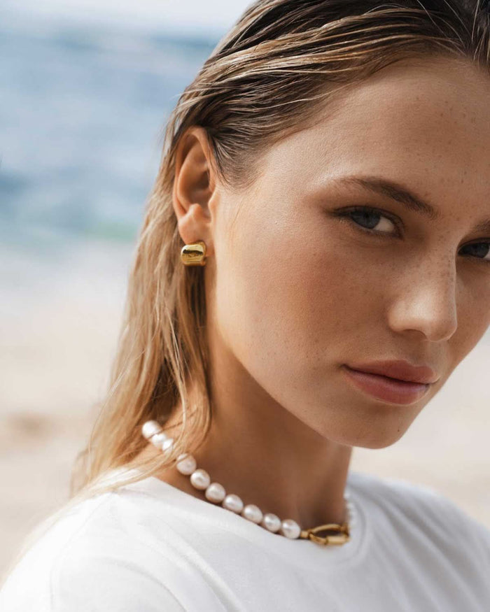 small gold earrings styled with a chunky pearl necklace