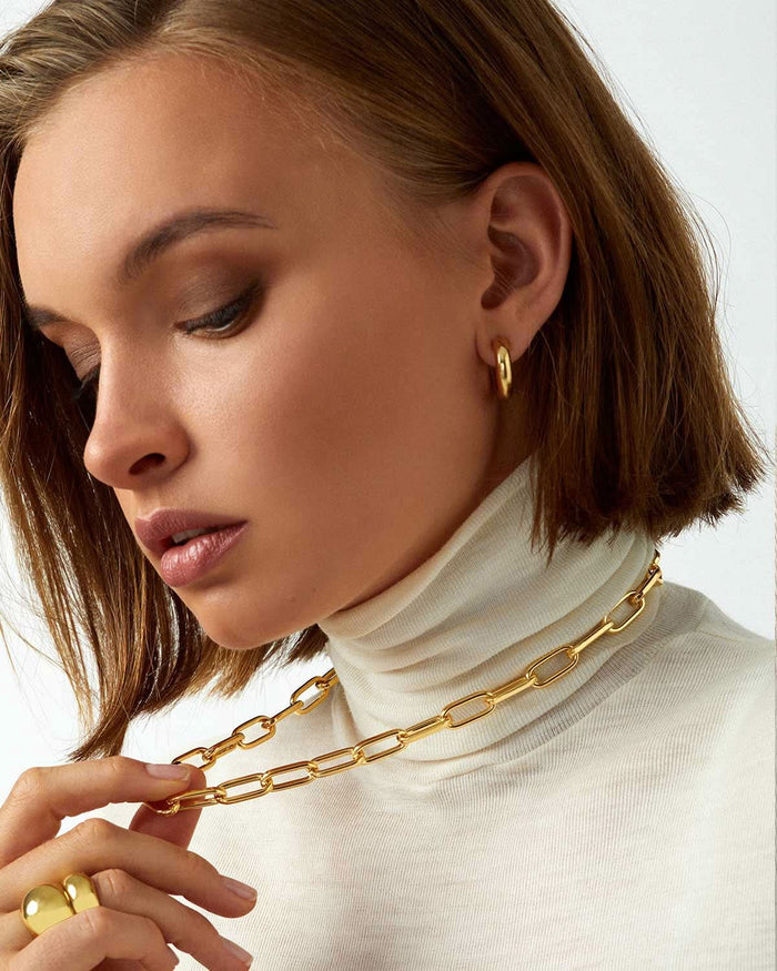 model profile wearing white turtle neck shirt with gold earrings, rings, and necklace