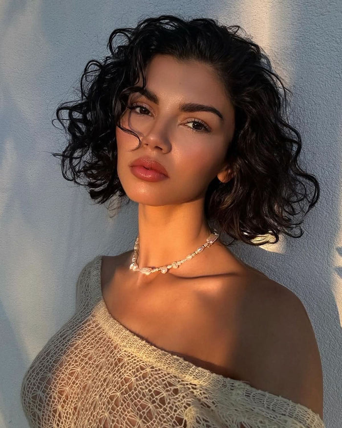 a girl next to the white wall wearing off shoulder top and pearl necklace choker