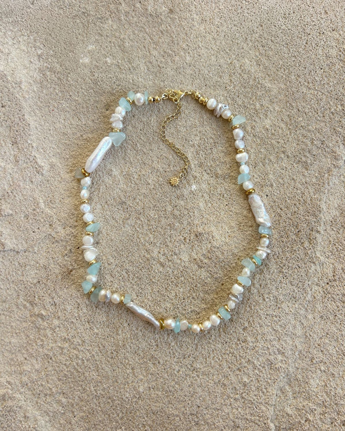 blue bead necklace with pearls on a beige stone surface