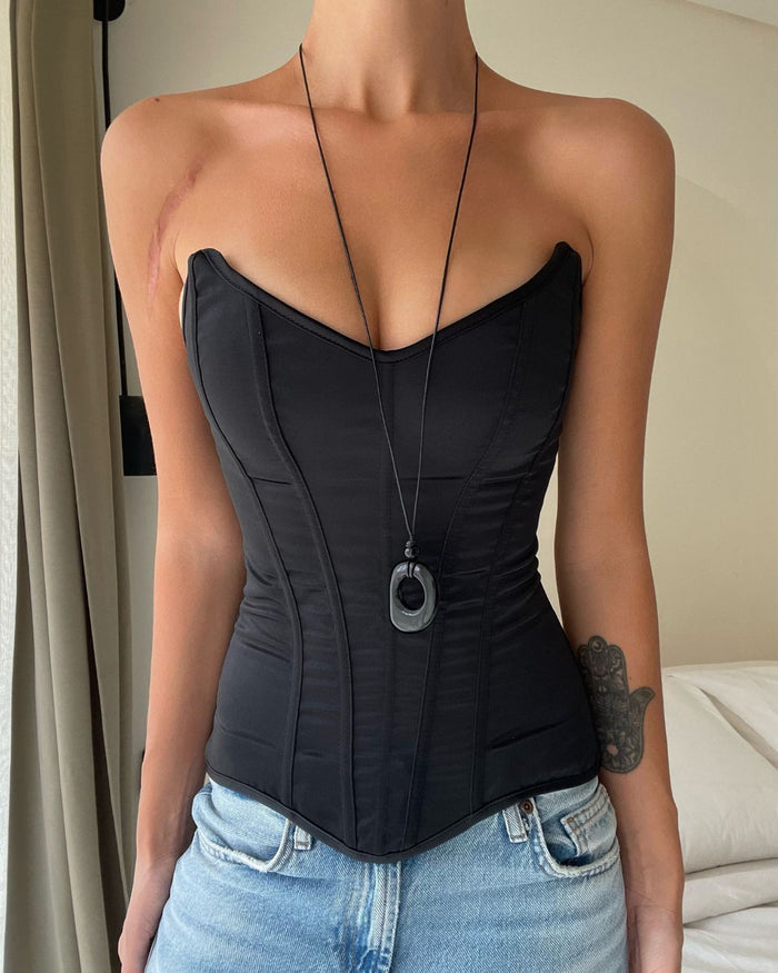 Cord necklace with a long black string and a black pendant over a black strapless corset top